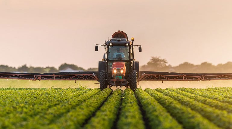 Tractor spraying on farmland at sunset